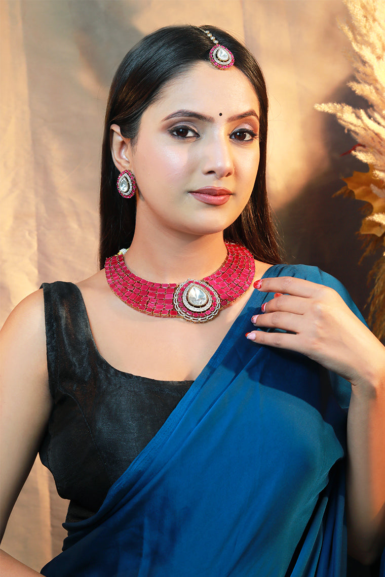“Woman wearing a pink stone choker necklace set with kundan centerpiece, matching earrings, and maang tikka.”