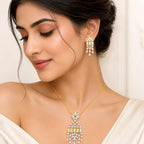 Luxury gold-tone crystal pendant necklace with matching chandelier drop earrings featuring baguette and pear-cut stones for bridal and party wear.