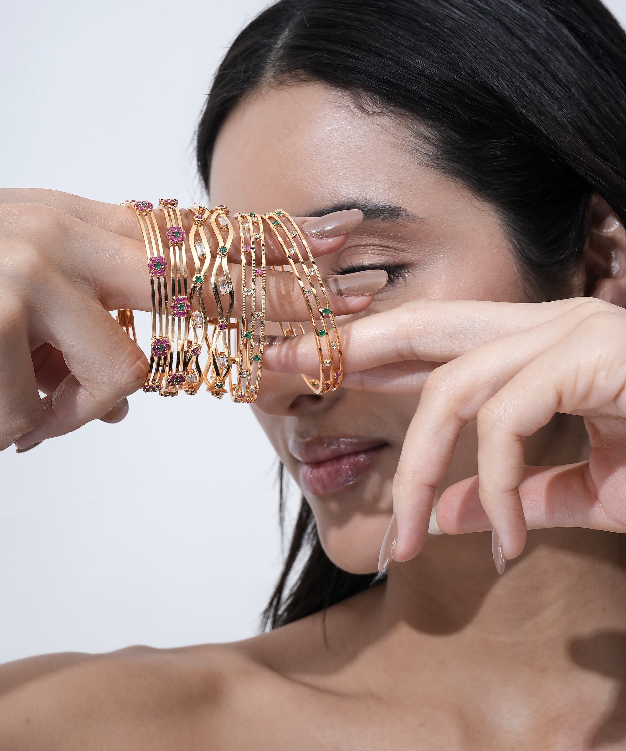 Gold-plated bangle set featuring pink, green, and white stone embellishments in elegant stackable designs.